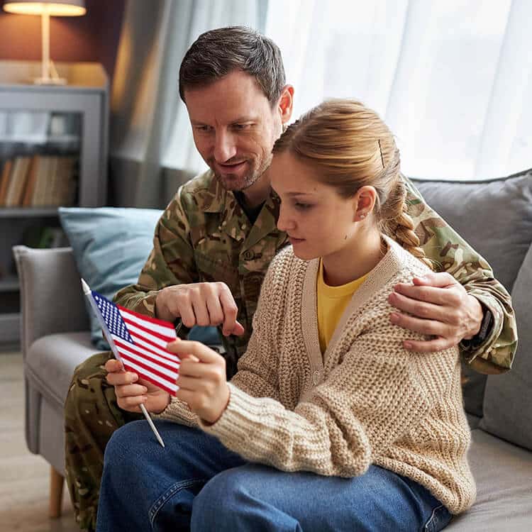 Army man sitting with daughter who is holding an American flag